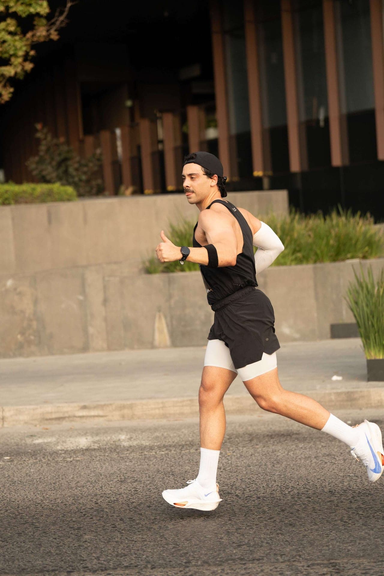 Wave One runner in a black singlet mid-stride on a city street, sun catching his shoes