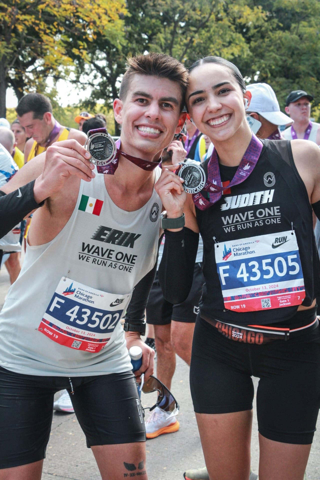 Two Wave One runners in white and maroon singlets showing their Chicago Marathon finisher medals