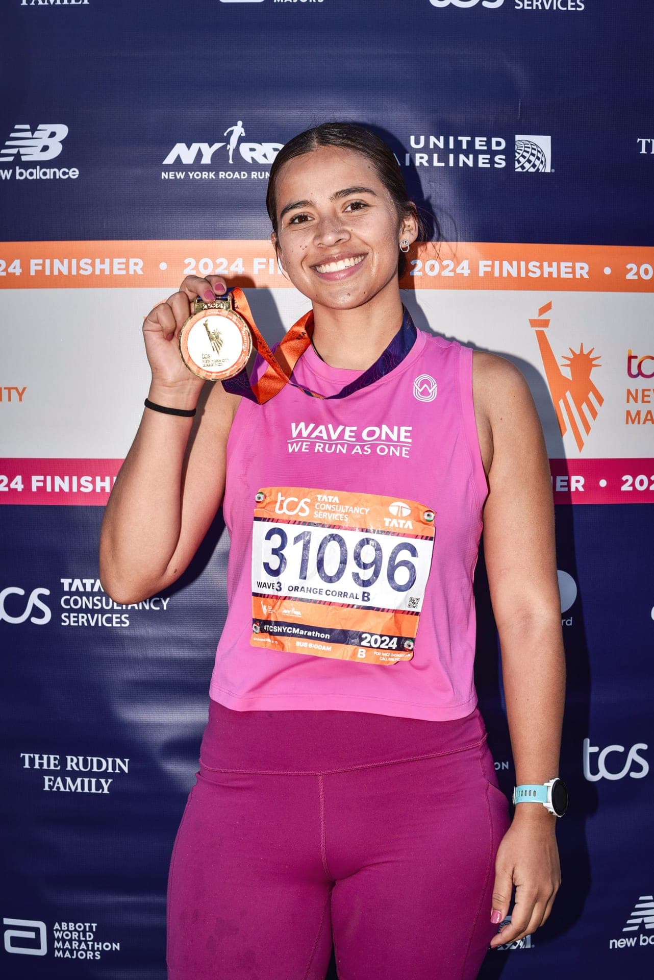Wave One runner in pink showing her NYC Marathon finisher medal at the photo wall