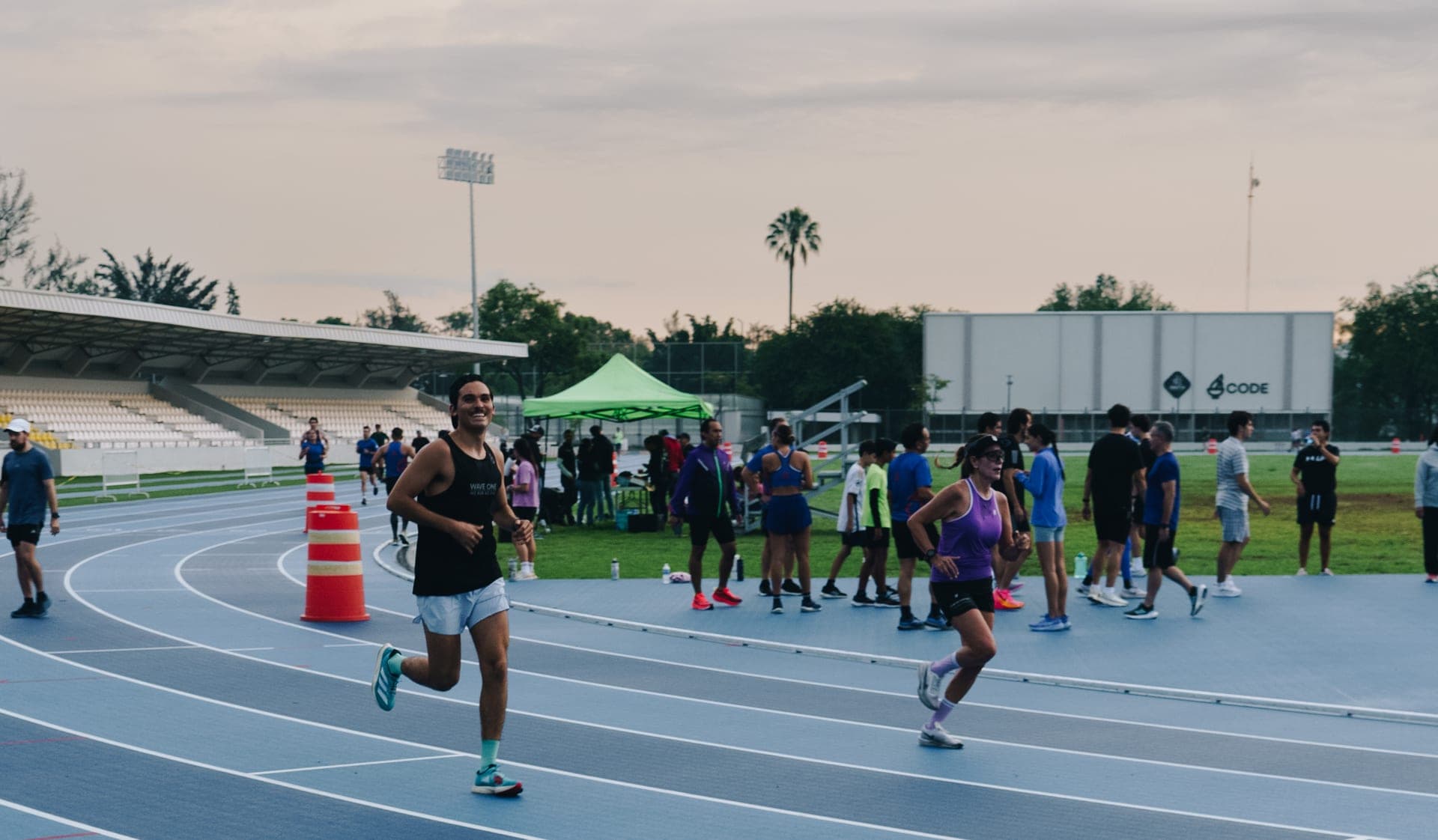 Smiling Waver in a black singlet rounding the bend of a busy track session at sunset