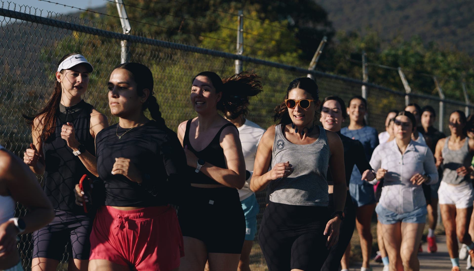 Group of women running side by side along a chain-link fence in golden morning light