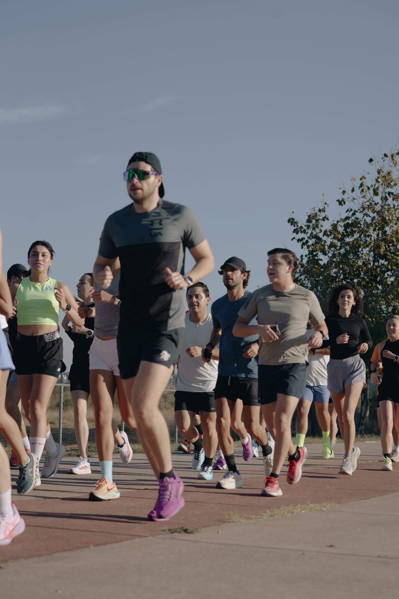 Lead pack of Wave One runners pushing forward on a sunlit path, colorful shoes and shades