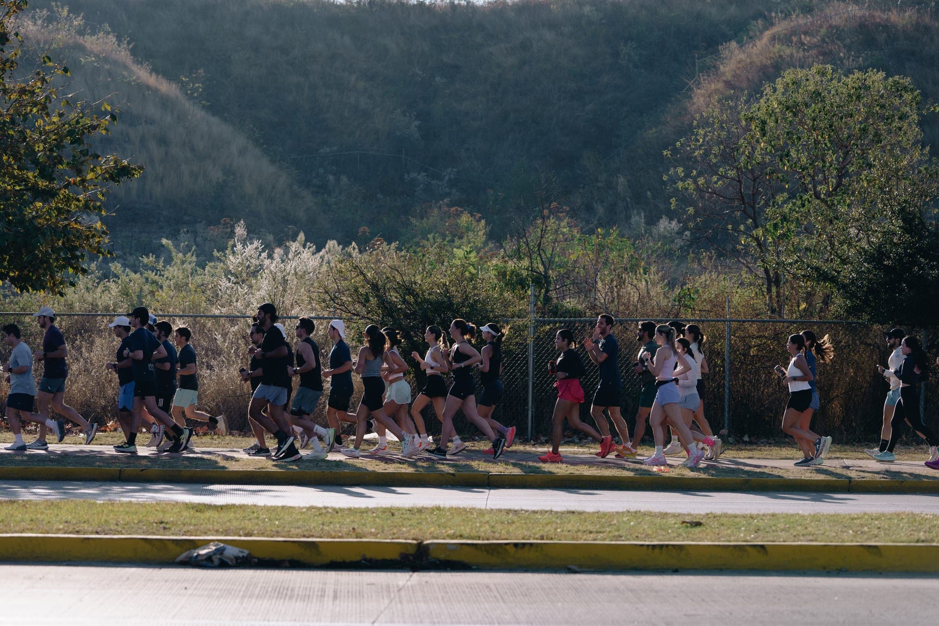 Long line of runners stretched along a roadside path with green hills in the background