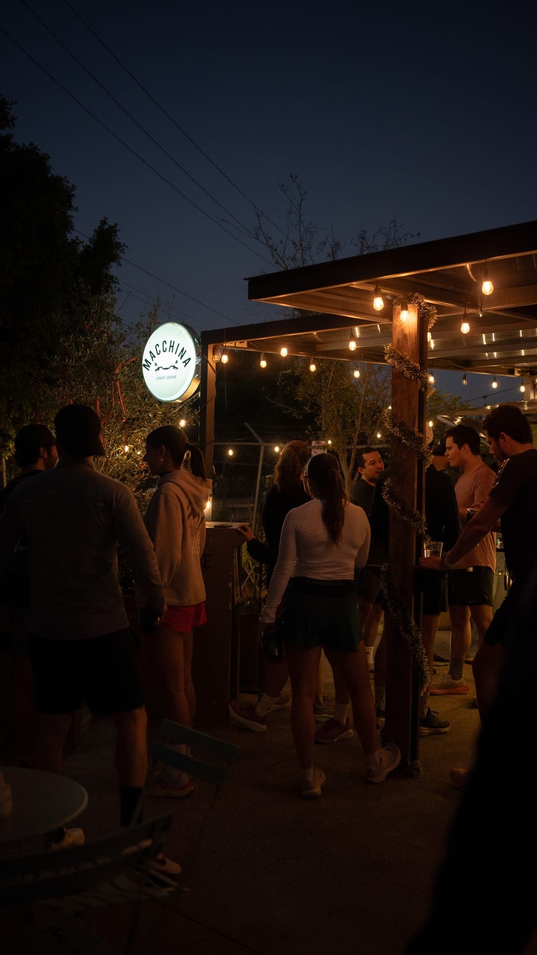 Cafe sign glowing at dusk as Wavers gather under string lights for post-run coffee